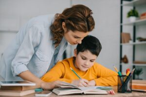 Beautiful woman standing near adorable writing in copy book while doing schoolwork at home